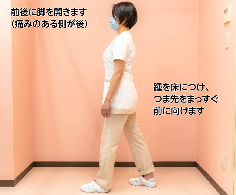 前後に脚を開きます（痛みのある側が後）。踵を床につけ、つま先をまっすぐ前に向けます