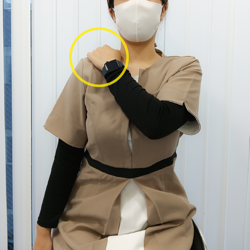 椅子に座った状態で、片方の手を反対側の肩に置きます。